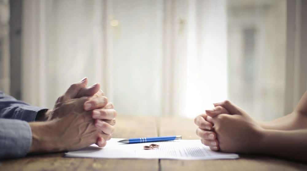 filing for divorce in Los Angeles County California portrayed by 2 people completing divorce paperwork with rings sitting on the papers.